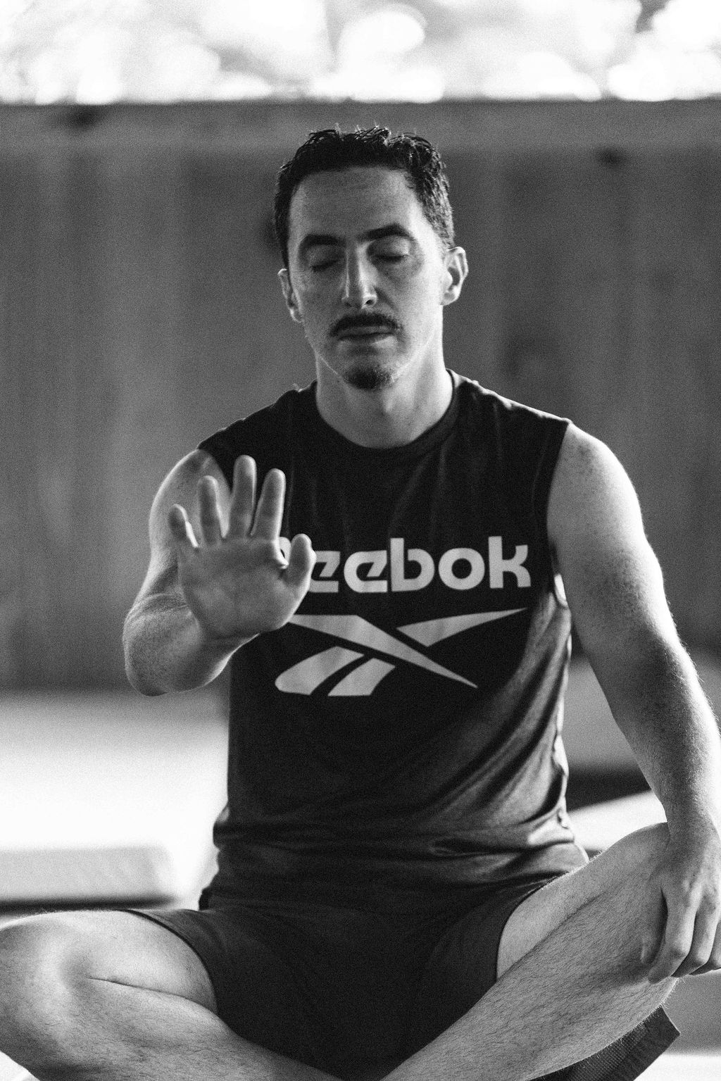 A man seated with his eyes closed and one hand raised